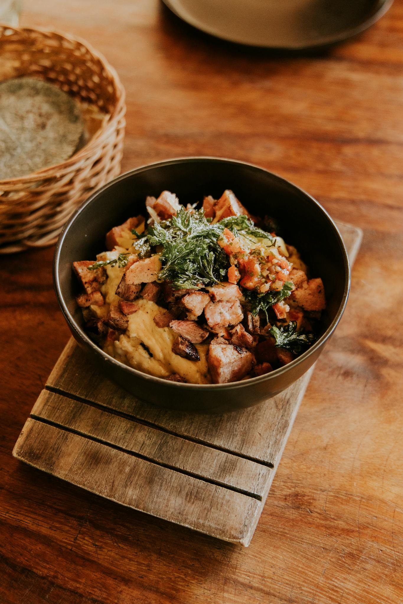 A warm and hearty dish featuring vegetables and protein, served in a rustic black bowl on a wooden table.