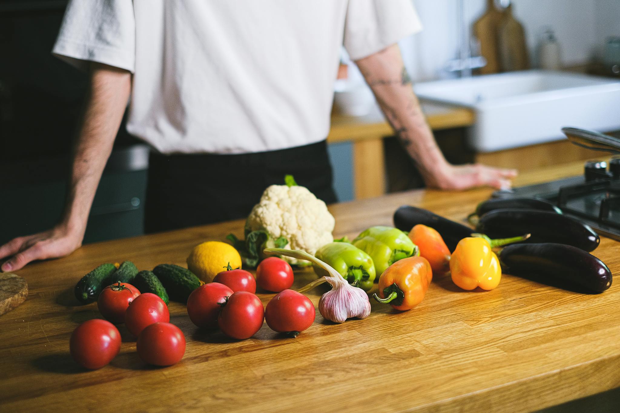 Diverse fresh vegetables on kitchen countertop with a person in the background. Perfect for healthy lifestyle content.